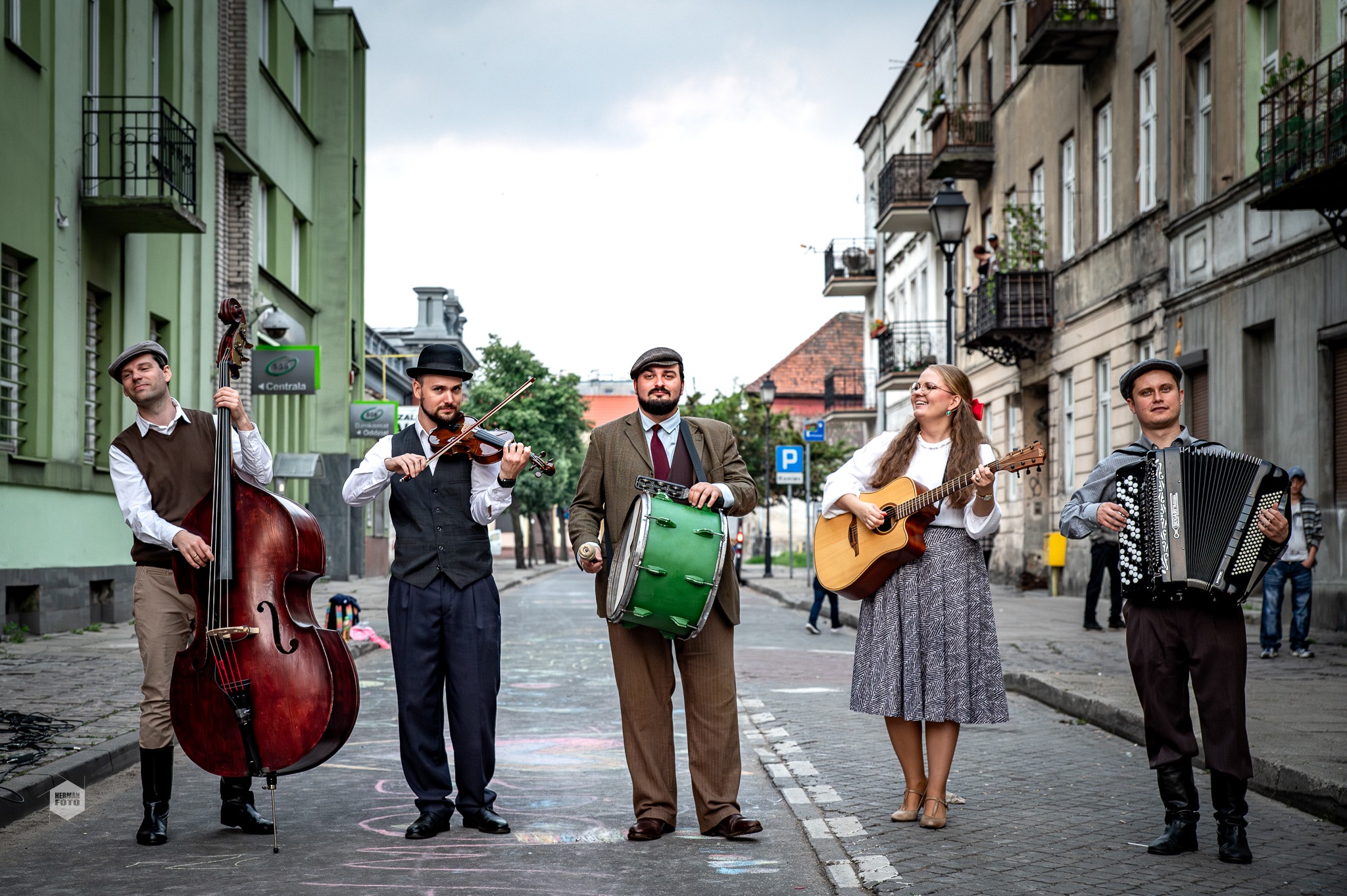 Czterech mężczyzn i jedna kobieta stoją na środku ulicy i grają na instrumentach muzycznych.