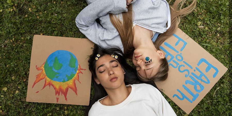 Dwie dziewczyny z zamkniętymi oczami leżą na trawie, przy głowach leżą rysunki, związane z ochroną ziemi.