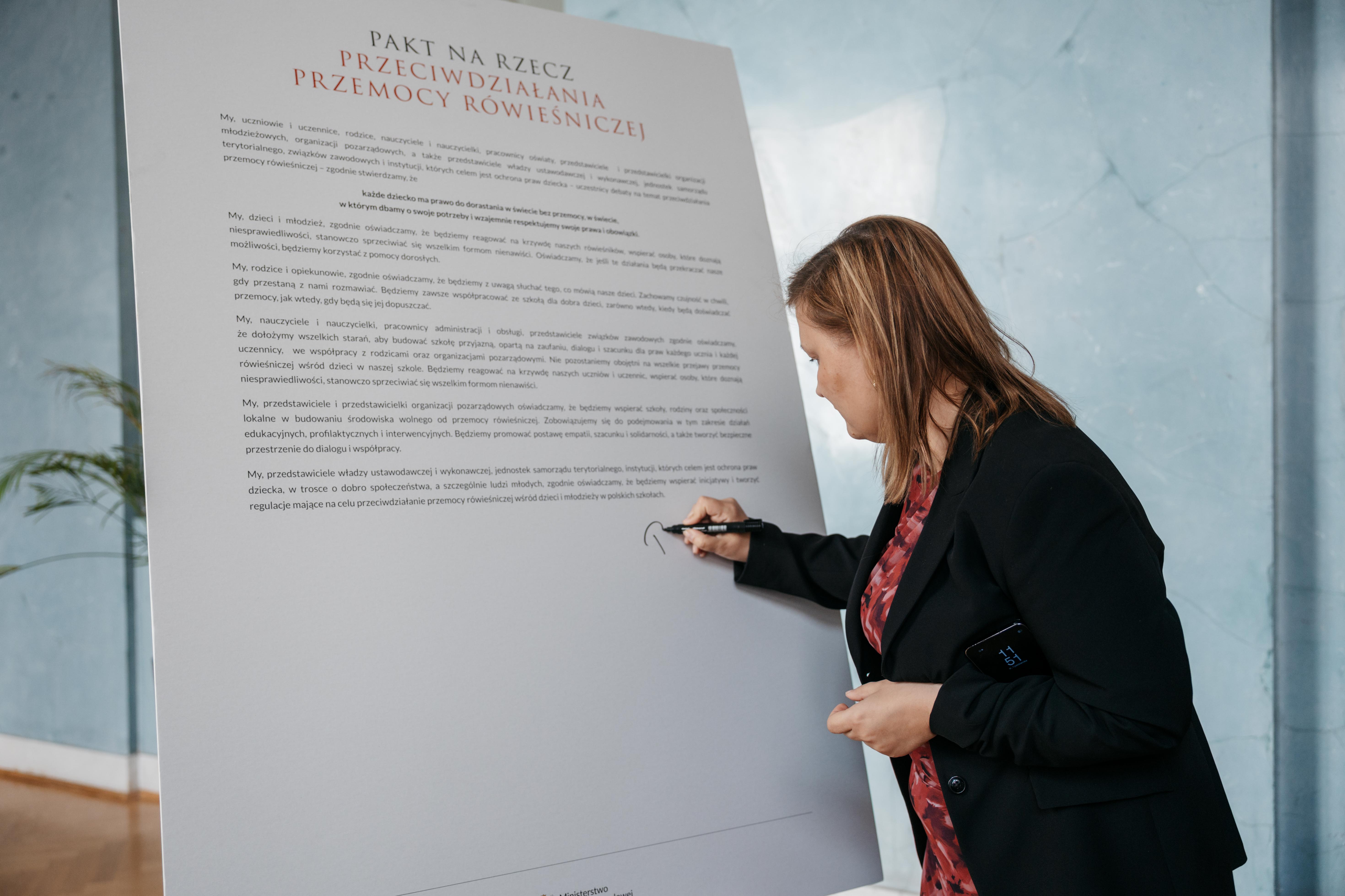 Kobieta składa podpis na tablicy pod treścią Paktu.