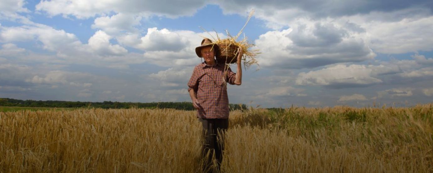 Mężczyzna z koszem na ramieniu w otoczeniu łanów zbóż.