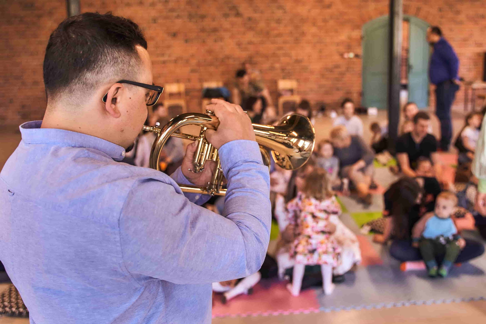 Mężczyzna gra na trąbce, w tle widać dzieci.