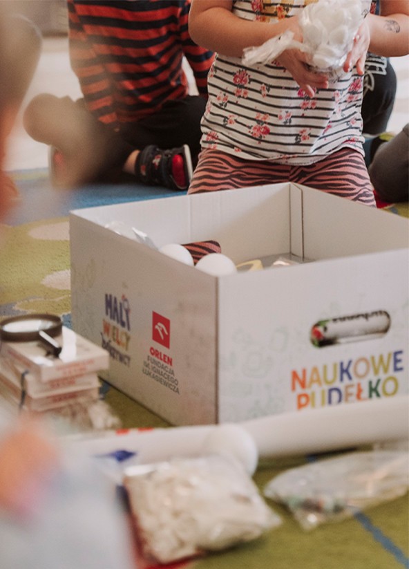 Przedszkolaki zgromadzone wokół kartonu z napisem 