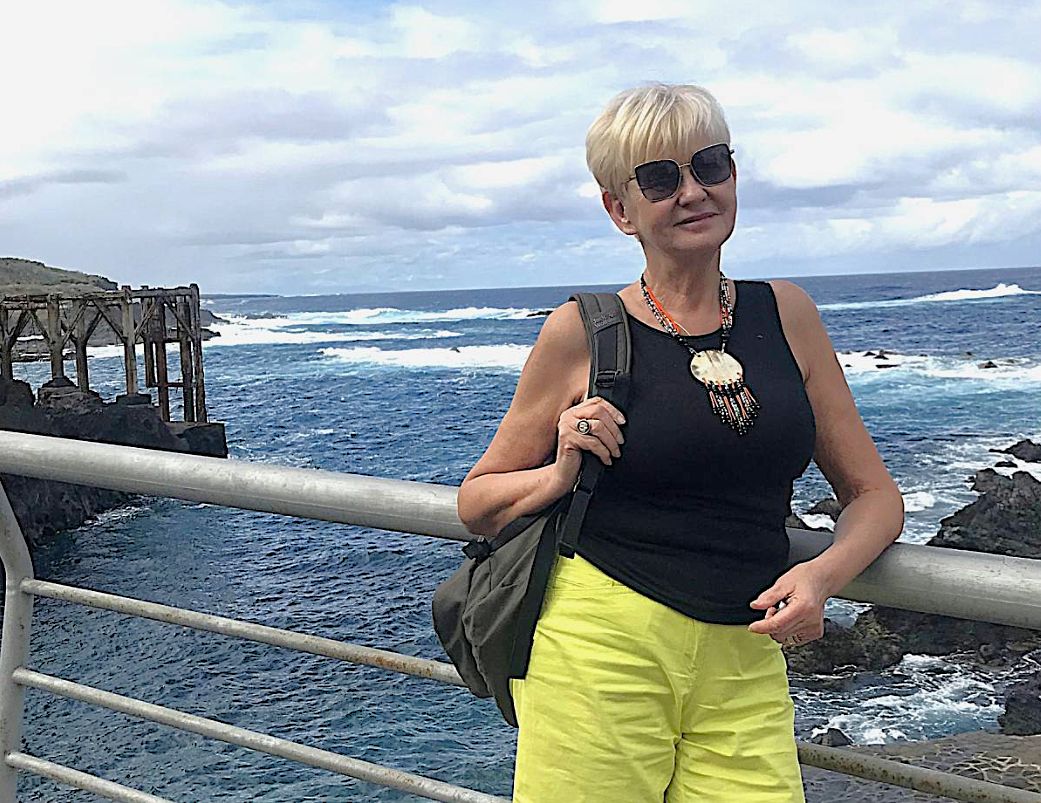 Kobieta w okularach przeciwsłonecznych pozuje nad brzegiem morza.