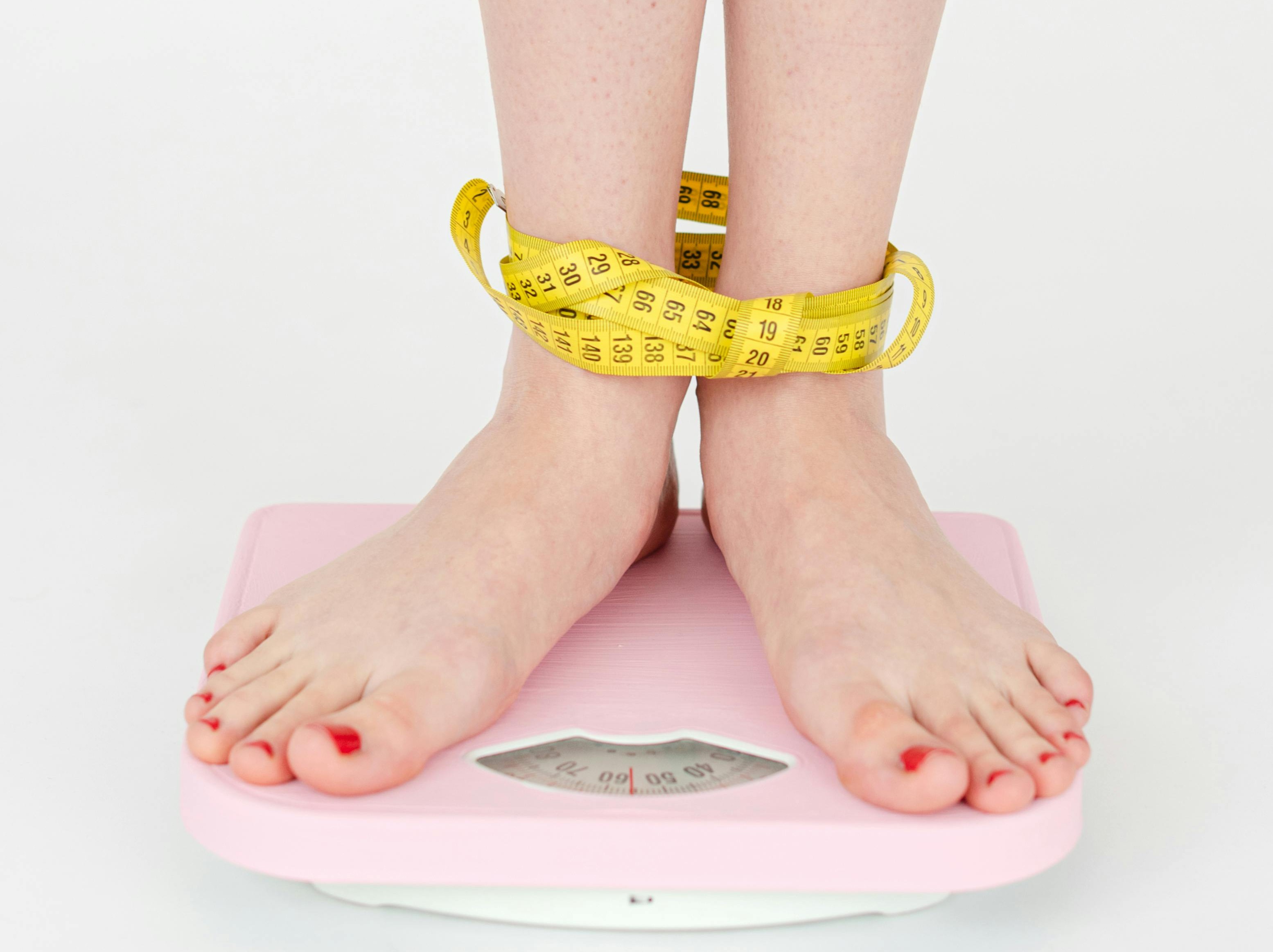 Waga domowa, na niej nogi dziewczyny, które są owinięte miarą krawiecką.