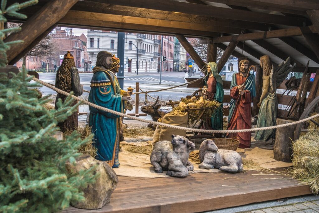 Uliczna szopka świąteczna z drewnianymi figurami ludzi i zwierząt.