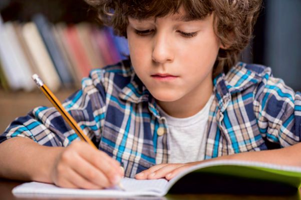 Chłopiec pisze ołówkiem w zeszycie.