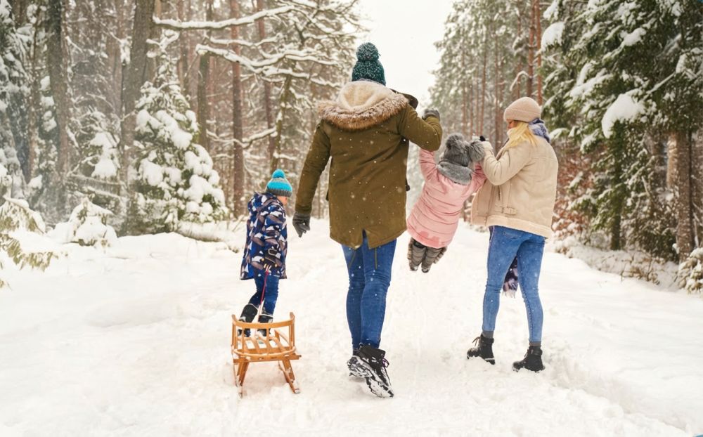 Rodzice i dwoje dzieci na zaśnieżonej drodze leśnej z sankami.
