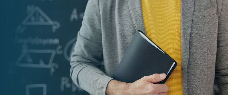  Fragment sylwetki mężczyzny trzymającego zeszyt.