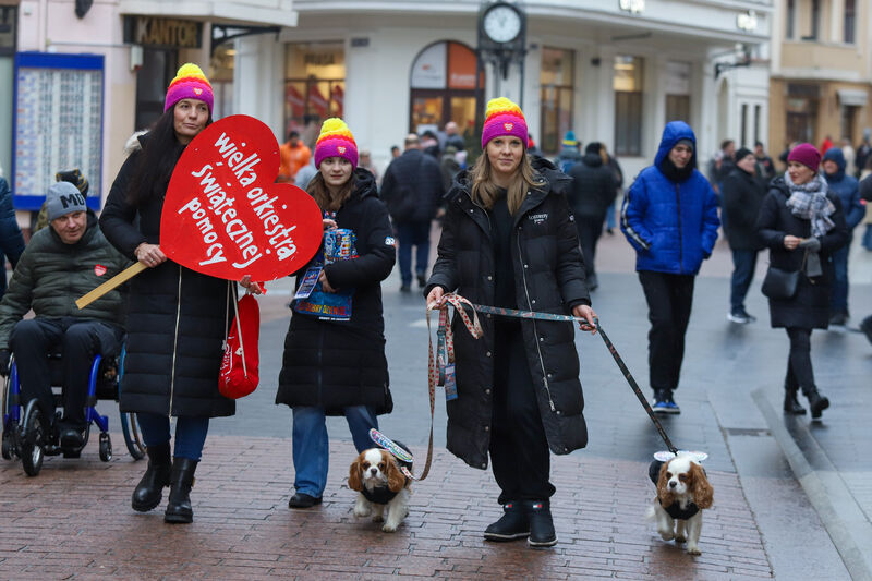 Trzy młode kobiety idą deptakiem z dwoma pieskami oraz  dużym sercem WOŚP.