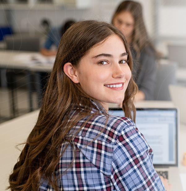 Uśmiechnięta uczennica przed komputerem w klasie.