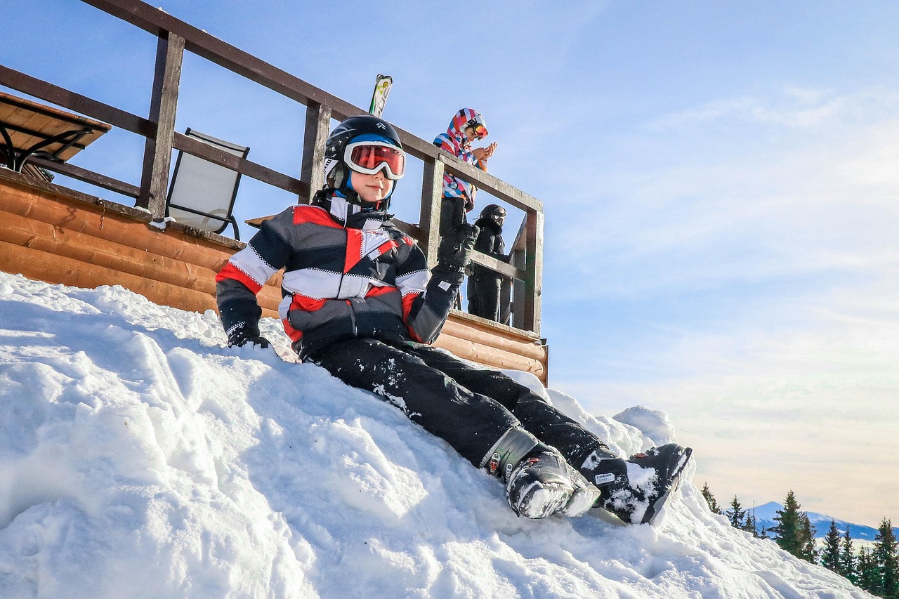Chłopiec w stroju narciarskim siedzi na śniegu w górach.