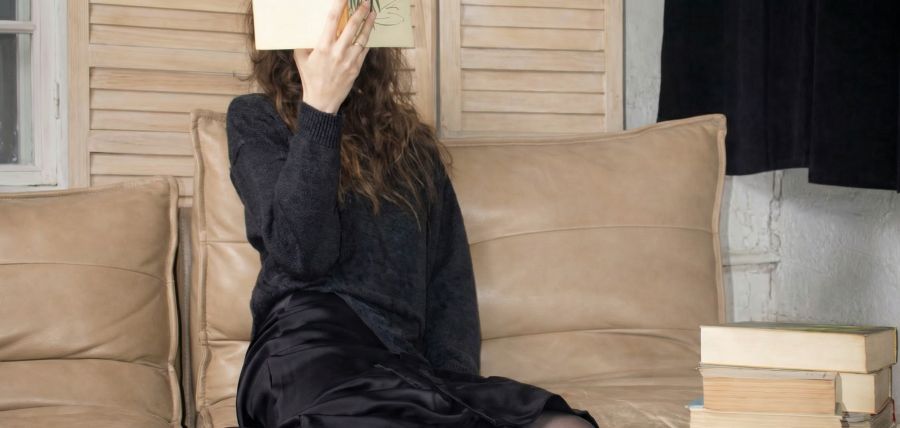 Kobieta z kanapie czyta książkę.