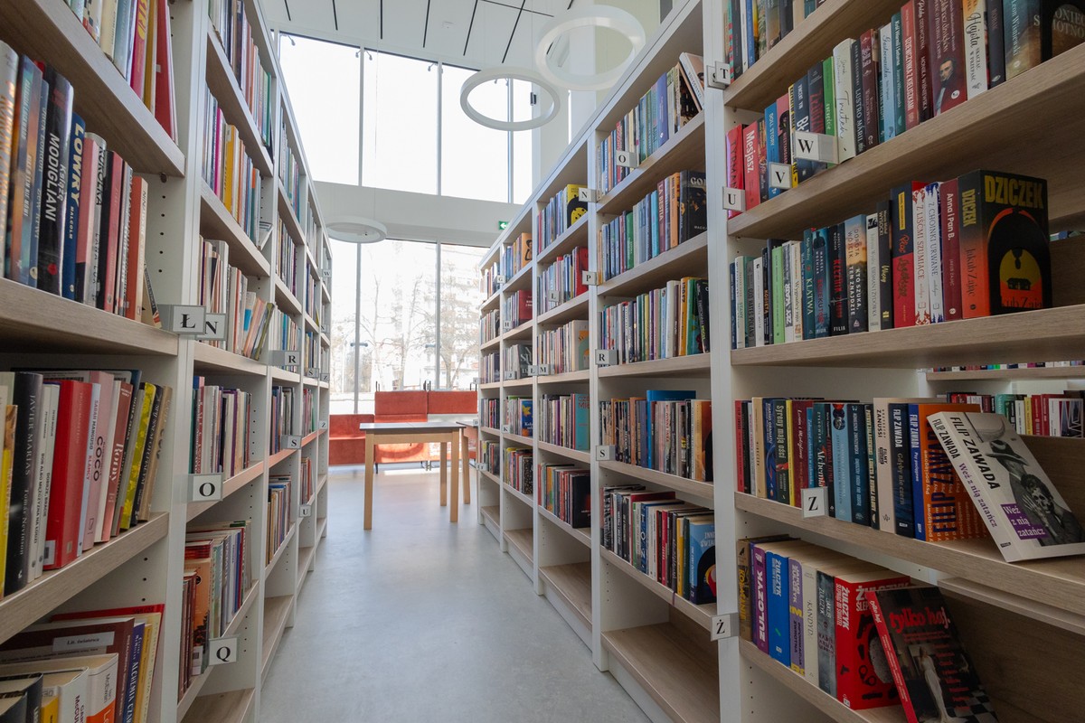 Nowoczesna, przestronna przestrzeń biblioteki, białe regały z książkami, w tle kanapy.