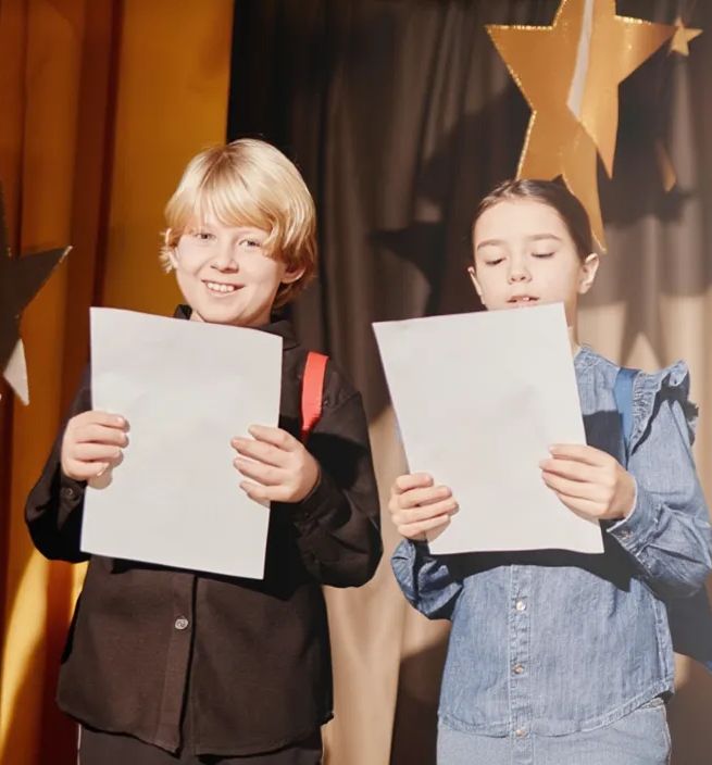 Dzieci trzymają teksty w rękach na scenie.