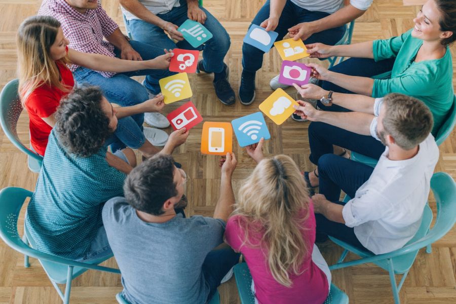 Osoby siedzące w kręgu trzymają przed sobą kartki z piktogramami.