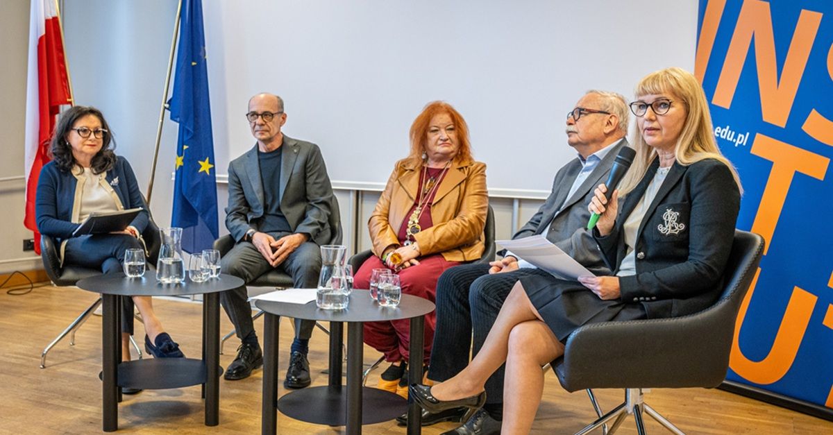 Uczestnicy debaty siedzą w fotelach przy stolikach. Kobieta trzyma mikrofon.