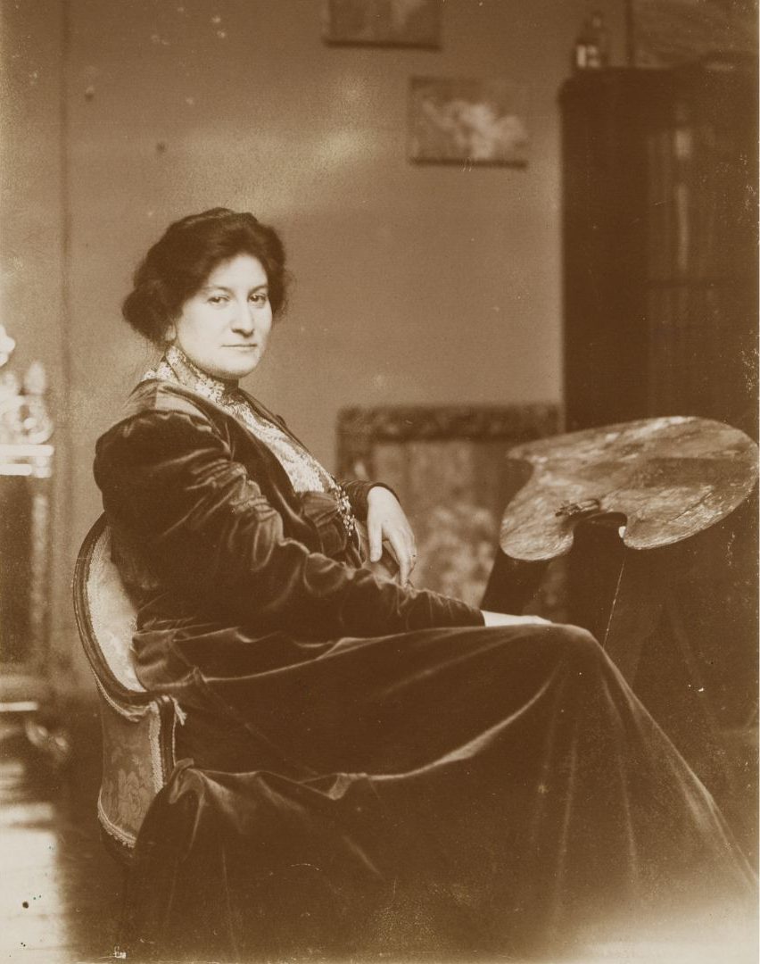 Kobieta na starym zdjęciu siedzi w ciemnej sukni.