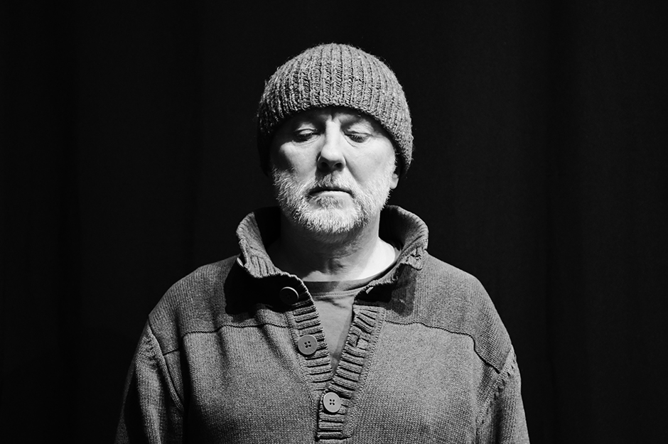 Mężczyzna w czapce, patrzący w dół, na czarno-białym zdjęciu.