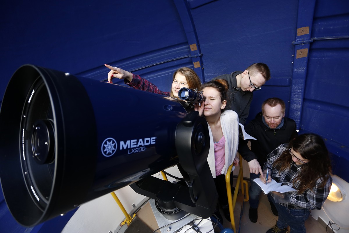 Młodzież patrzy przez teleskop, jedna osoba robi notatki.