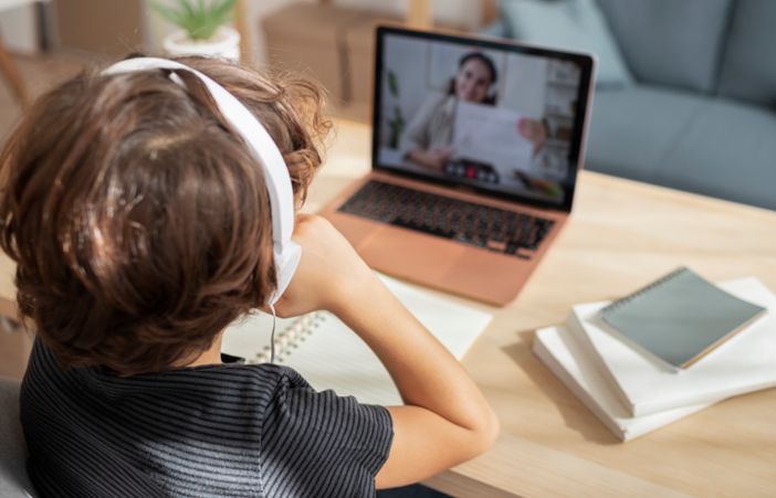 Chłopiec w słuchawkach przed laptopem podczas lekcji zdalnej.