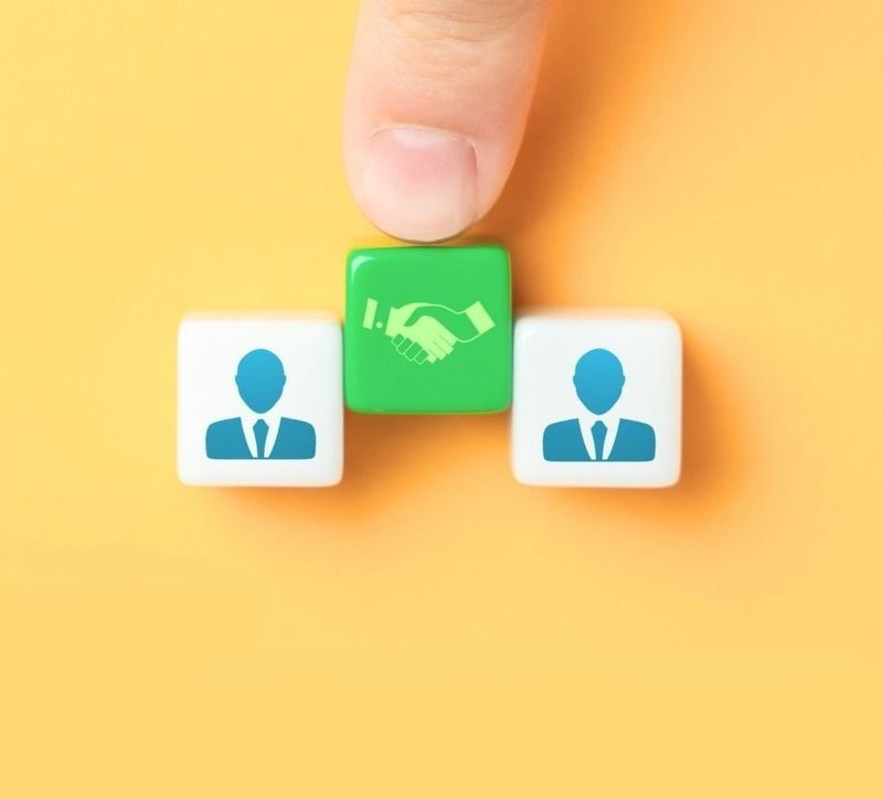 Pomiędzy klocki z piktogramami mężczyzn dłoń wsuwa klocek z uściskiem rąk.