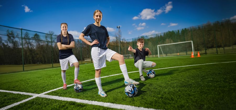 Dwie dziewczyny i chłopak na boisku piłkarskim.