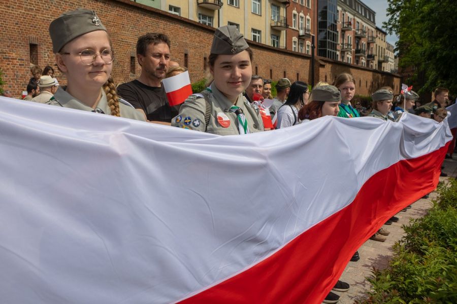 Harcerze i dorośli z flagami i chorągiewkami w barwach narodowych.