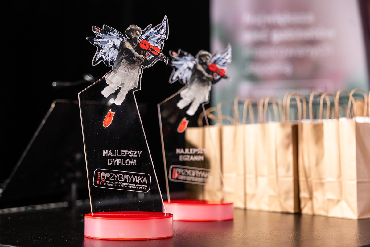 Statuetki festiwalowe dla nagrodzonych z motywem toruńskiego Flisaka z czerwonymi skrzypcami, w tle torebki prezentowe.