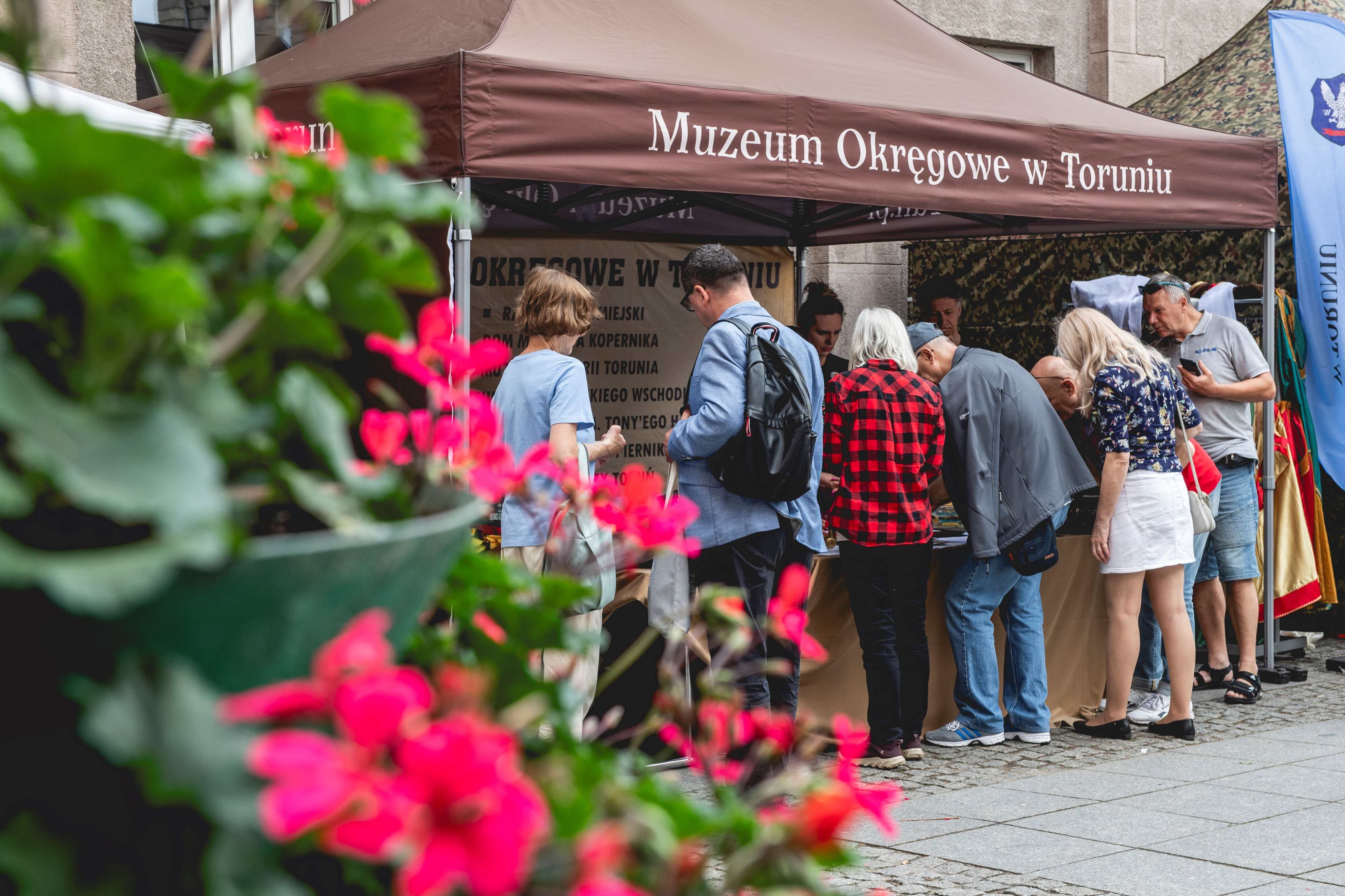 Stoisko Muzeum Okręgowego w Toruniu, przy którym gromadzą się ludzie.