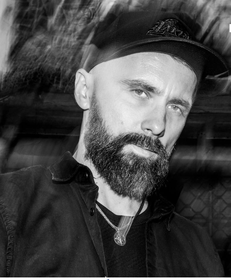 Mężczyzna z brodą i wąsami, w czapce z daszkiem.