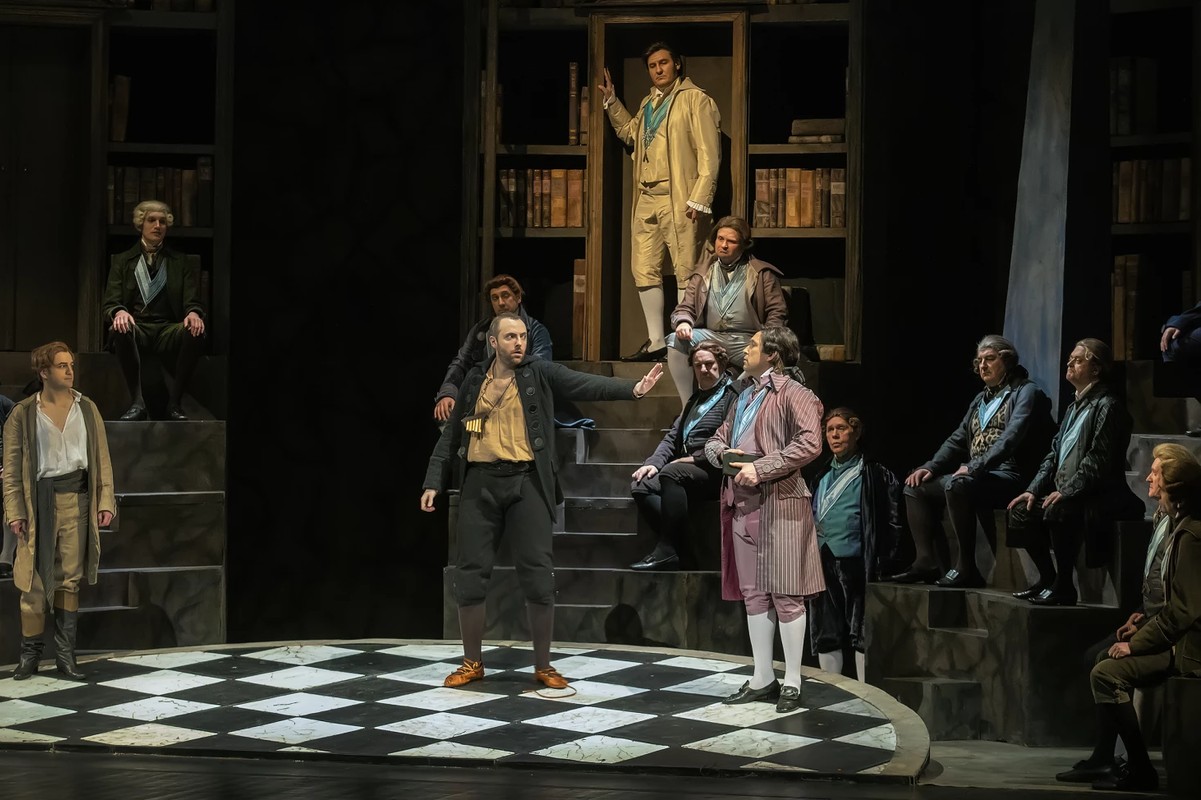 Grupa mężczyzn na scenie, w tle regały ze starymi księgami