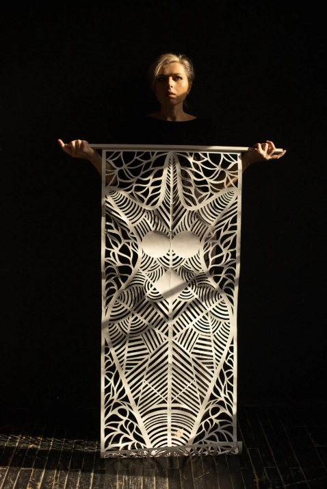 Zdjęcie kobiety trzymającej w dłoniach dużą wycinankę z papieru.