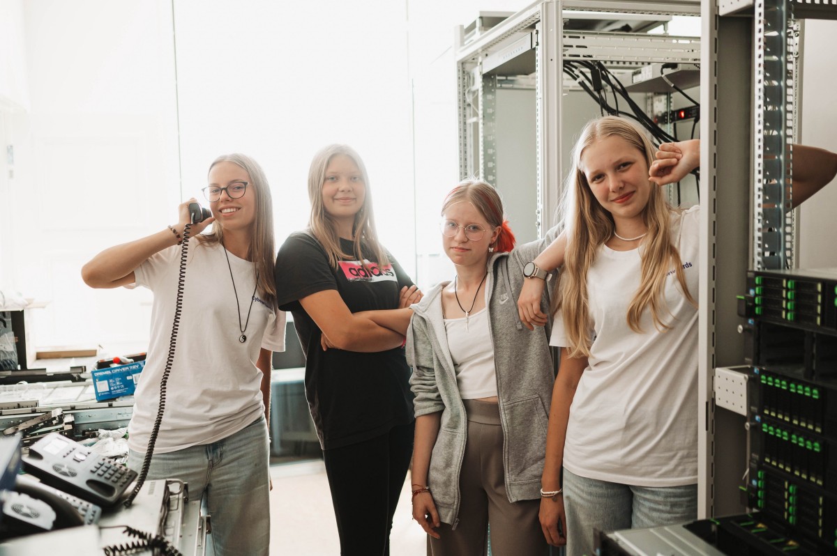 Cztery uśmiechnięte dziewczyny stoją w pomieszczeniu biurowym.