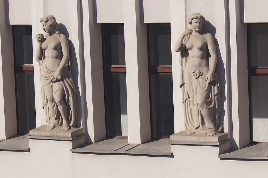 Dwie rzeźby kobiece w całej postaci na elewacji kamienicy.