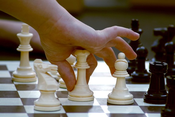 dziecięca ręka rozgrywająca białym pionkiem szachów