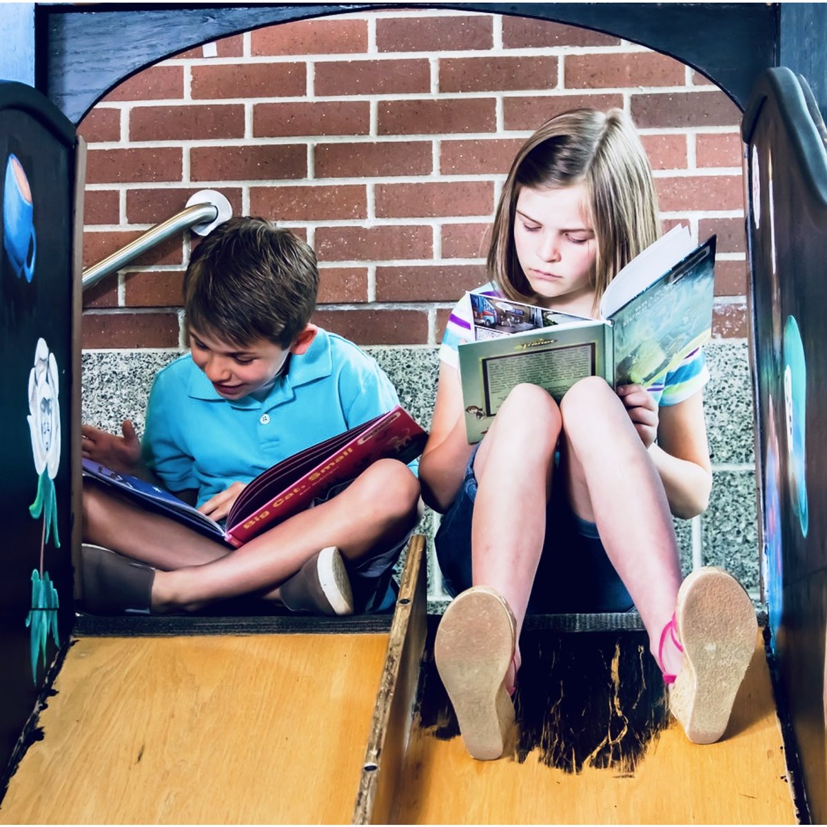 Dziewczynka i chłopiec czytają książki siedząc na zjeźdżalni