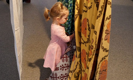 Kilkuletnia dziewczynka ogląda różnokolorowe tkaniny