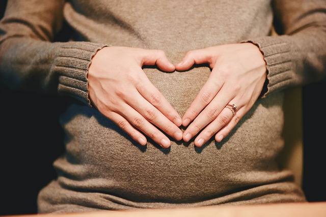 kobieta w ciąży trzyma dłonie na brzuchu; stykające się palce kobiety tworzą kształt serca