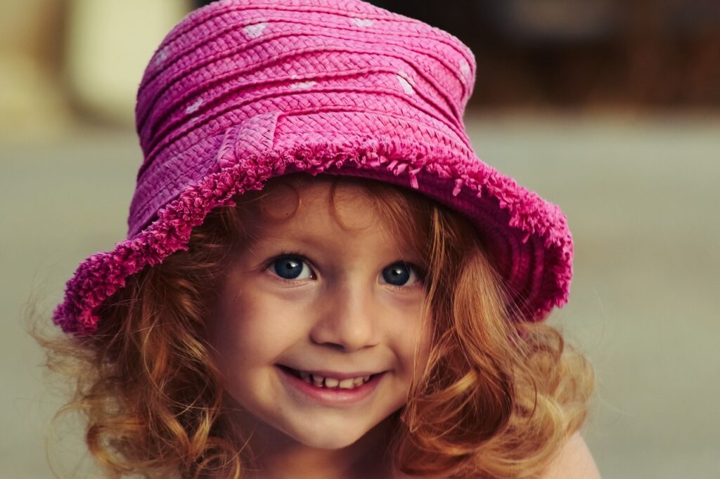 Uśmiechnięta mała dziewczynka o blond kręconych włosach w różowym kapeluszu