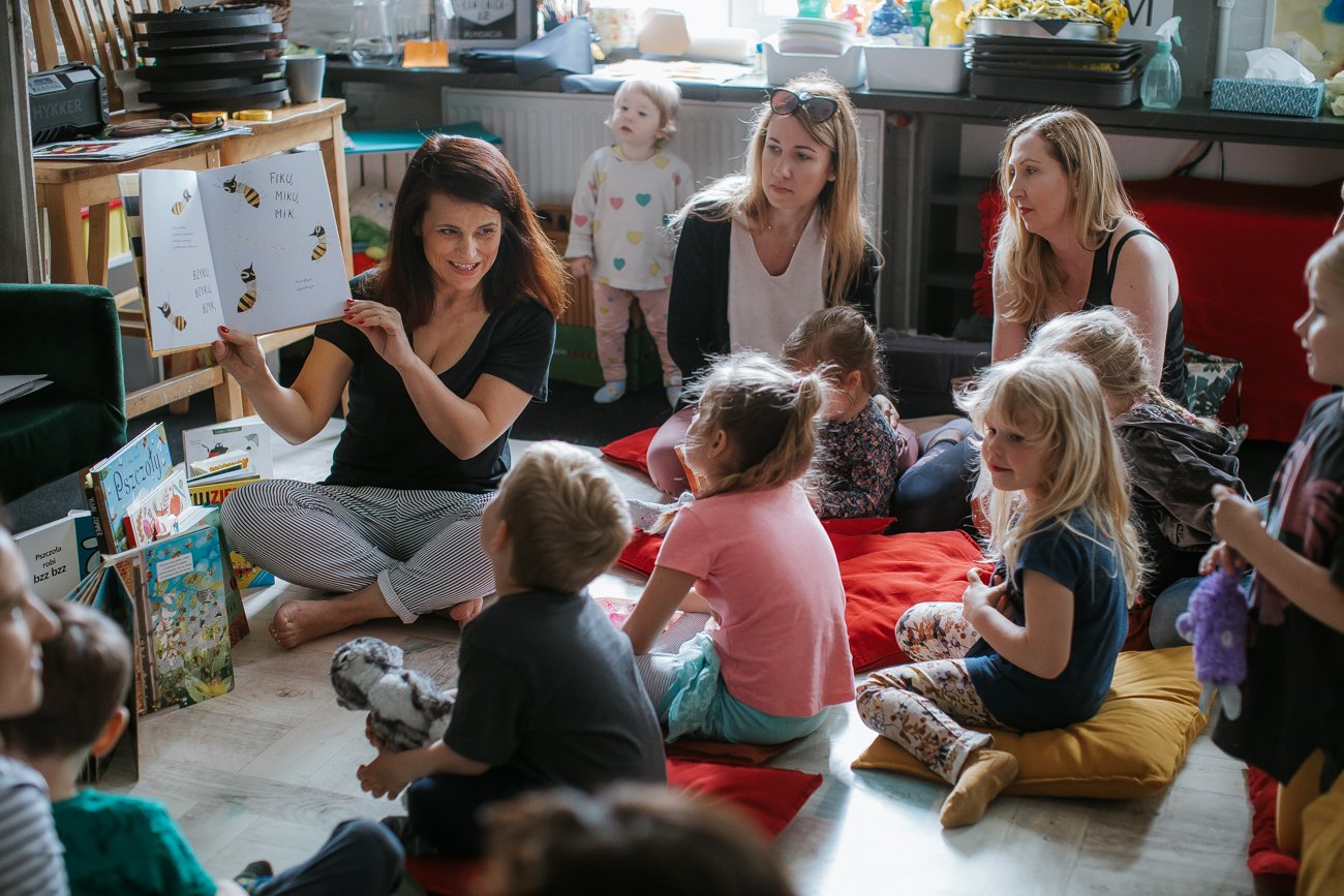 Dzieci i kobiety siedzą na podłodze i patrzą na otwartą książkę.