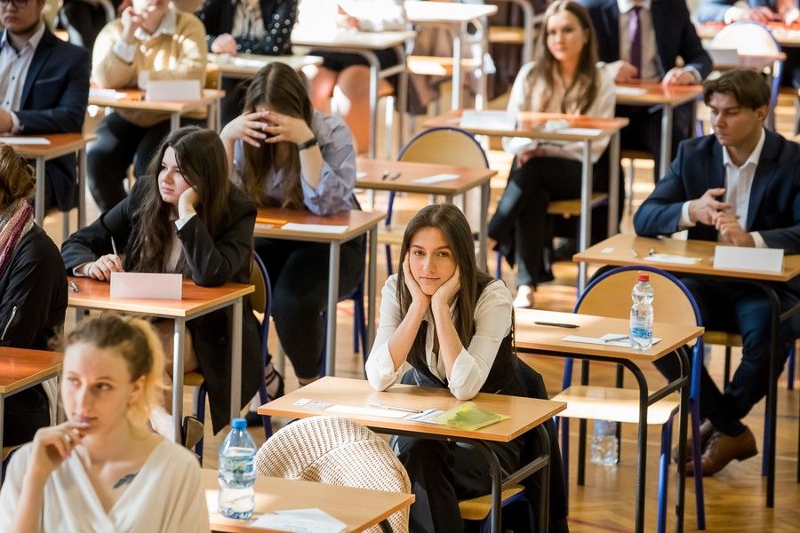 Elegancko ubrana młodzież siedząca przy stolikach podczas egzaminu maturalnego