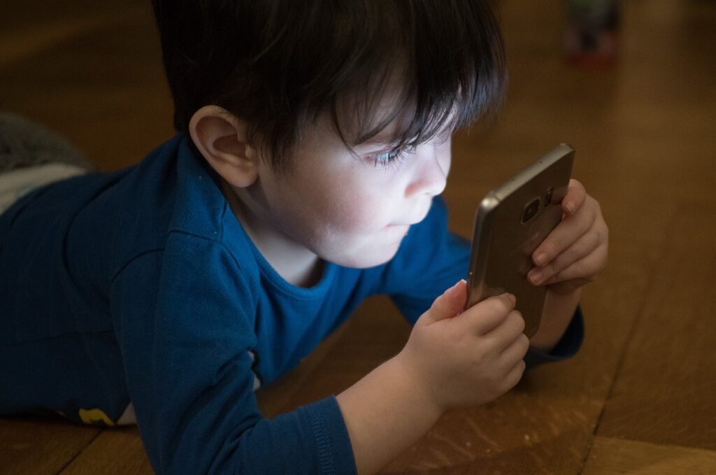 Mały chłopiec w ciemnym pomieszczeniu patrzy w rozświetlony ekran telefonu