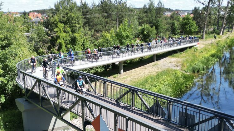 Grupa rowerzystów przejeżdża most dla pieszych i rowerzystów.