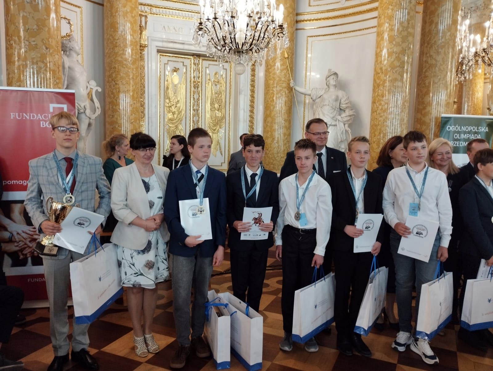 Grupa uczniów odbiera nagrody w Sali Wielkiej Zamku Królewskiego w Warszawie.