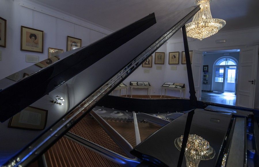 elegancka sala Ośrodka Chopinowskiego w Szafarni, na pierszym planie otwarty fortepian, w tle szklany żyrandol, obrazy na ścianach