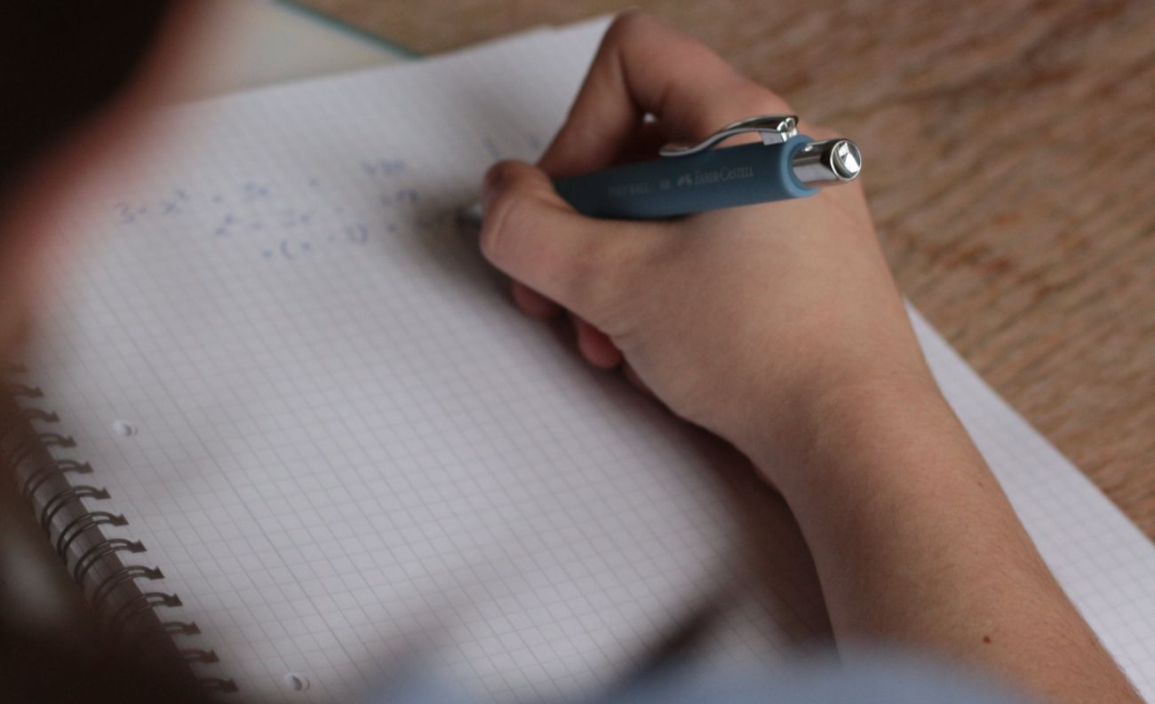 Dłoń z długopisem nad notatnikiem z zadaniem matematycznym.