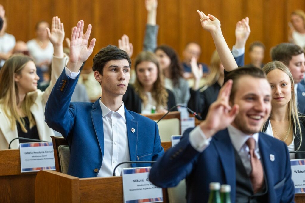 Młodzież: kobiety i mężczyźni głosują z podniesionymi rękami w sali Sejmiku