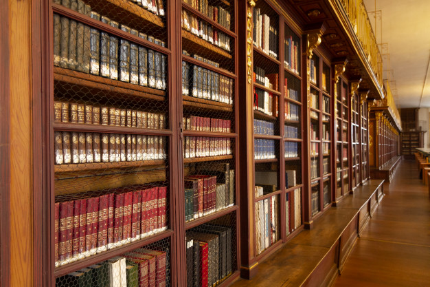 Rząd starych regałów bibliotecznych z oprawionymi tomami.