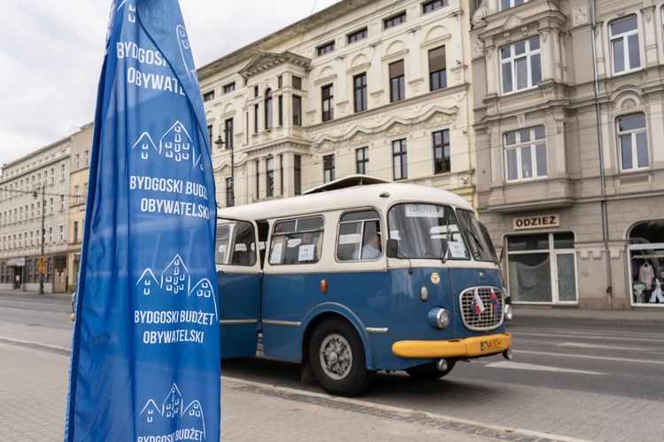 Zabytkowy autobus Jelcz w kolorze niebieskim. W tle miejskie kamienice.