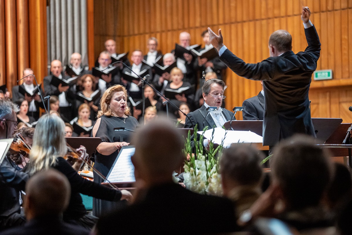 koncert orkiestry symfonicznej z solistką i chórem, na pierwszym planie znajdują się tyłem orkiestra i dyrygent